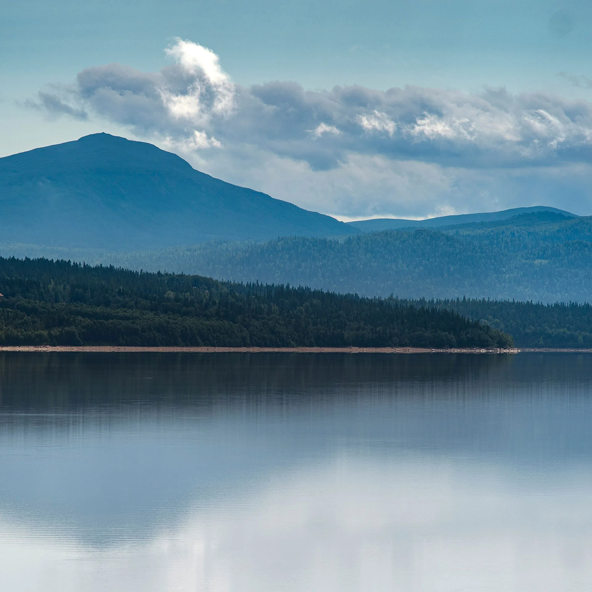 Naturbild över sjö med fjäll och blå himmel i bakgrunden
